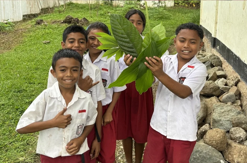 Siswa membawa daun dari kebun ke kelas.